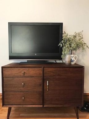 A dark walnut midcentury modern TV console with 3 drawers on its left side, and a cabinet on its right. A TV and small vase of flowers sit on top.